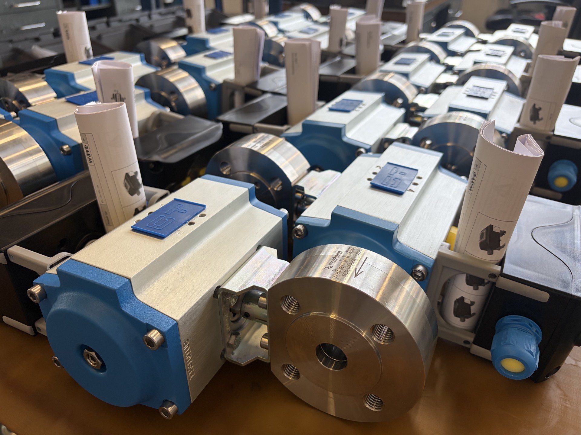 Folge 11_Schnappschuss - vonScheven Close-up of blue and silver industrial rollers in a production machine, with rolled sheets and manuals visible on each unit